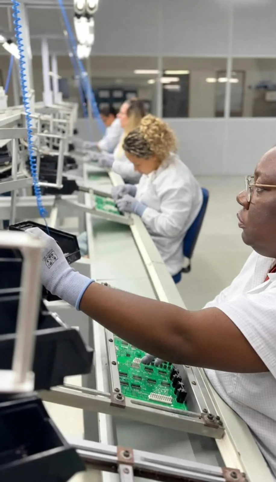 Operadoras conferindo placas eletrônicas na bancada da linha de montagem